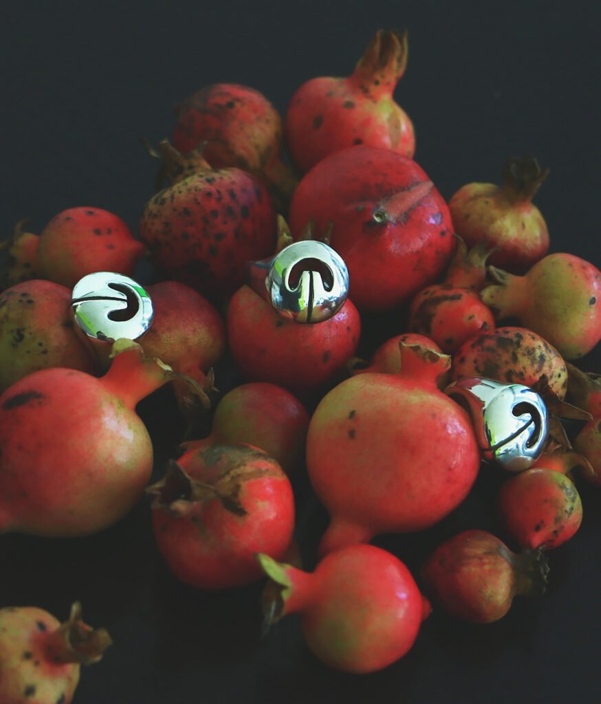 Multiple silver Lingling-o rings displayed on ripe pomegranates — symbols of fertility and abundance meet sacred ancient design