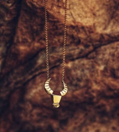 Gold Carabao water buffalo necklace displayed on mountain rocks – artisan talisman of grounded strength and cultural heritage