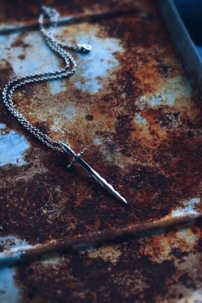 Silver Katipunan sword necklace set against a rusty industrial backdrop – symbol of Filipino resilience and historical strength, handcrafted in Spain.