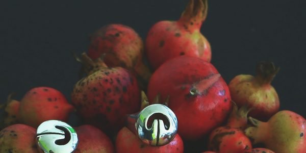 Multiple silver Lingling-o rings displayed on ripe pomegranates — symbols of fertility and abundance meet sacred ancient design