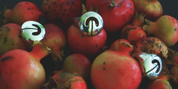 Multiple silver Lingling-o rings displayed on ripe pomegranates — symbols of fertility and abundance meet sacred ancient design